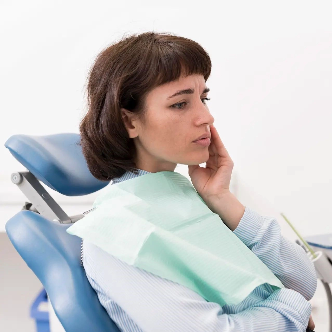 A young woman sitting in a dentist's chair, holding her face in discomfort.